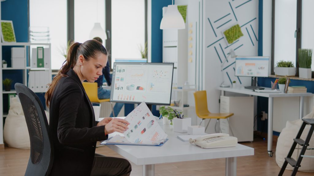 Mujer de negocios buscando CRM para PYMES Entre libretas y ordenador en una colorida oficina. 