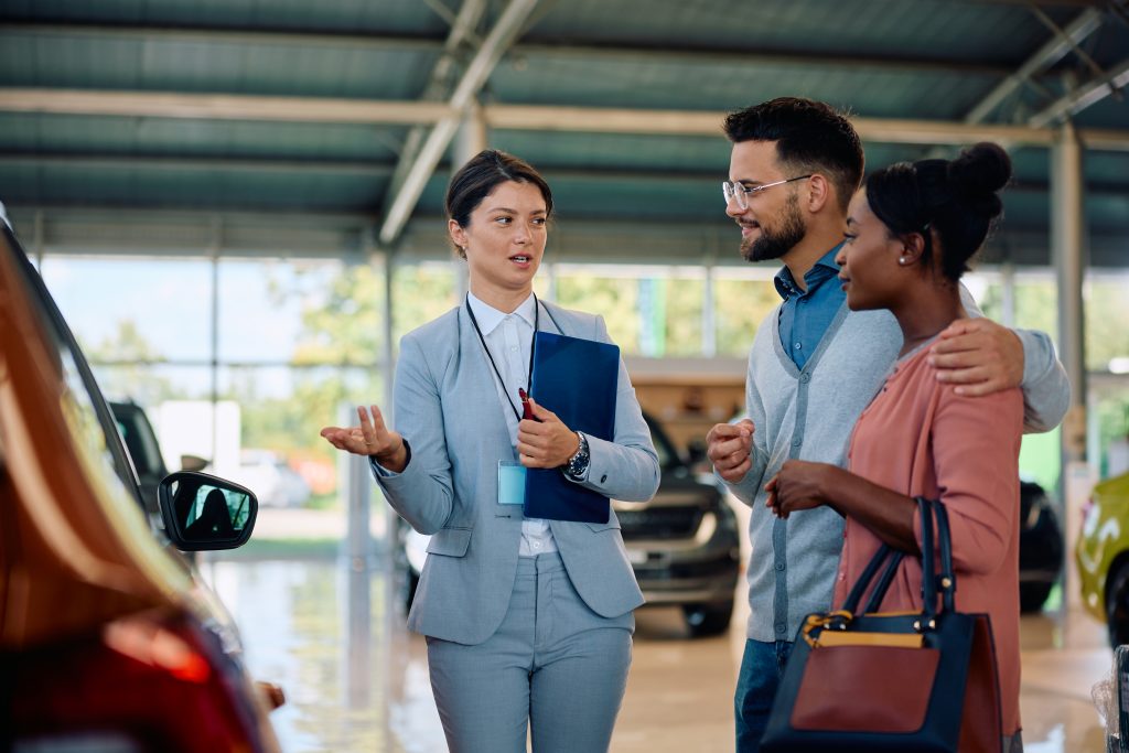 Mujer vende coche a pareja mientras indica con la mano.