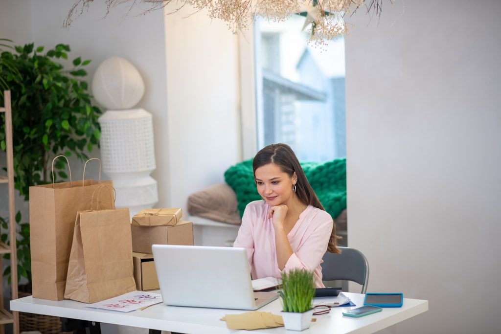 Mujer realiza speech de ventas ejemplos en el ordenador mientras prepara el seguimiento de ventas con muchos paquetes a su lado